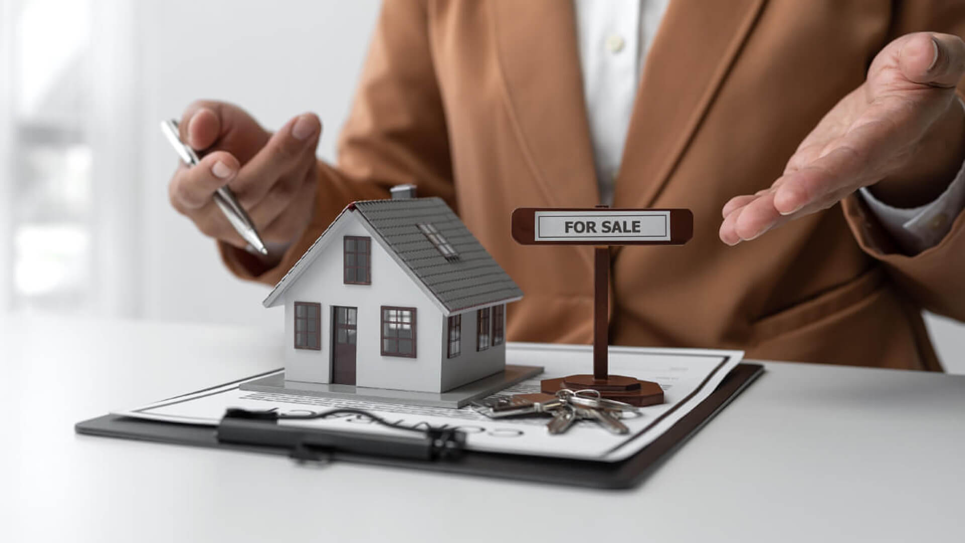 Hands placing a 'For Sale' sign on a model house representing the sale of rented property in Dubai